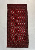 Full view of the rectangular hand knotted wool Turkoman mat rug on a white surface showing overall pattern and colors.