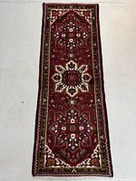 Full length view of a hand knotted Persian Heriz runner rug with deep red background and geometric medallions, laid flat on floor.
