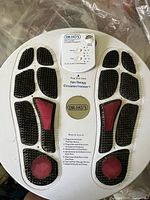 Top view of Dr Ho's Pain Therapy Circulation Promoter device with black and red textured footpads shaped like footprints and the brand logo.