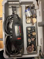 Black Dremel Moto-Tool rotary tool with power cord, various grinding and polishing bits in a gray molded plastic case.