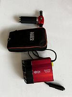 Photo of Mac Tools red and black handheld butane torch, black Klein Tools carrying case, and Tripp-Lite red 150W power inverter with car plug cord.