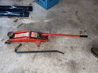 Full side view of the red Motomaster hydraulic trolley jack with a long handle and wheels, showing general condition and design.