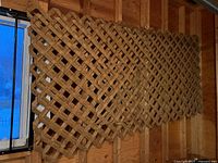 Four wooden lattice panels hanging vertically in an indoor unfinished wood walled room. Two large panels and two smaller square panels are visible.