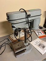 Side view of the gray metal Mastercraft drill press, showing the main body, motor housing, lever handles, and adjustable table with slots.