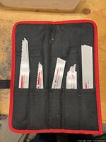 Close-up of five reciprocating saw blades in a black fabric holder with red trim, showing varied tooth designs and 'The Torch' branding.