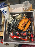 View of the plastic bin containing an orange jig saw, Jobmax rotary tool, white Imperial wrench roll with wrenches, and red c-clamps.
