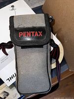 Grey Pentax-branded fabric camera case with black trim and red lettering