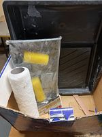 Photo showing black paint tray, yellow foam rollers, and white textured roller in a cardboard box