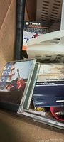 Various CDs and printed item including a Timex box in a cardboard box.