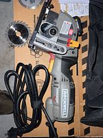 Photo of Rockwell Versacut mini circular saw showing side profile, laser guide, and two extra circular blades placed nearby.