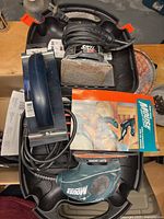 Photo showing the Black & Decker Mouse hand sander, Skil power sander, sanding pads and paper inside plastic carrying case