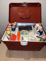 Open brown sewing supply case showing white insert tray with various sewing threads on spools and small sewing accessories