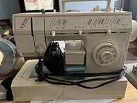 Full front view of the Singer sewing machine with power cord wrapped around the base and foot pedal attached.
