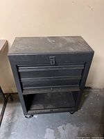 Front view of the black metal tool chest, showing the drawers and open lower cabinet section and casters under it.