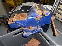 Large blue bench vise with rusted jaws and surface wear, showing entire vise including swivel base and handle