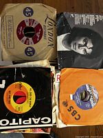 Top view of four 45 RPM vinyl records with their paper sleeves showing various record labels and cover art.