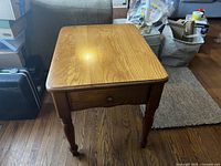 Front view of one wooden side table showing the rectangular top, drawer with round metal pull, and turned legs on wood floor.
