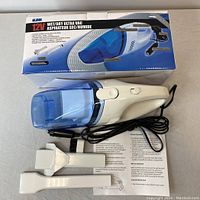 Photo of 12V Elink Wet/Dry Ultra car vacuum with power cord and two white attachments on a grey surface, including product box in background showing product details.