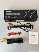 Full set showing Aimtom camera mounted on bracket, RCA and power cables, and user manual in original box.