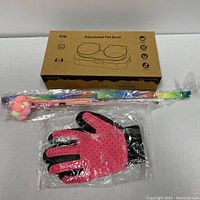 Cat Essentials Bundle including adjustable pet bowl set in box, colorful cat toys, and pink grooming glove in plastic packaging.