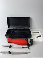 Red Cushore electric cutter with ergonomic handle, two blades, black power adapter, manual and black molded hard plastic carrying case with compartments for the items.