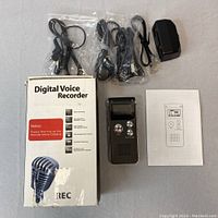 Digital voice recorder and accessories laid out beside the product box and manual.