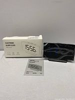 Electronic alarm clock in original box with manual featuring a digital time display 15:56 and product branding on the package.