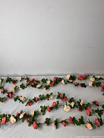 Five artificial floral garlands laid out horizontally showing alternating red and cream roses with green leaves against a white backdrop.