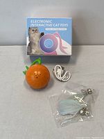 Photo of the electronic interactive cat toy in pumpkin shape, USB charging cable, and accessory with feathers and bells in plastic package, along with the product box featuring cat image and branding.