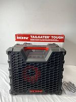 Front view of the ION Tailgater Tough speaker on top of its original box. Speaker features a black and gray rugged design with a red accent in the grille shape and handle. Box displays product name and key features.