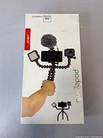Box front showing the Joby GorillaPod Mobile Rig held by a hand, mounted with a smartphone, light, and microphone.
