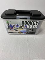 Front view of plastic game case with black lid showing 'Hockey Guys' branding featuring Bruins and New York Rangers teams.