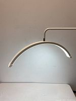 White floor lamp lit and showing the curved arc LED bar with bright white light, mounted on an adjustable arm and square base