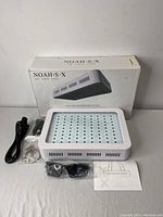 Noah SX LED grow light kit laid out with box, LED panel, hanging kit, power cable, and instruction sheet on table.