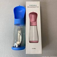 Portable dog water bottle with blue top bowl and clear body, placed beside box with pink bottle image and text "PORTABLE DOG WATER BOTTLE 510ML"