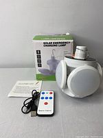 Solar Emergency Charging Lamp box, lamp, remote control, and USB charging cable displayed on a flat surface.