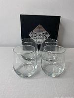Four stemless clear wine glasses displayed in front of a black box with "Glasses Nobility Series" label.