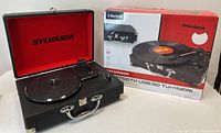 Overall view of the Sylvania turntable open with red-lined lid and original box showing product image and branding.