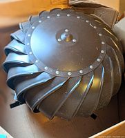 Roof turbine vent fan placed in a cardboard box, showing riveted top cover and curved turbine blades from above.