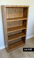 Photo showing a wood grain bookcase with 4 shelves and a small hole in the back panel on the top shelf.