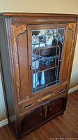 Photo showing full front view of wooden china cabinet with glass door and decorative metal panes, two drawers under glass door, and double door storage at bottom