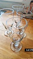 Photo showing four tall clear dessert glasses arranged in a cluster on a wooden surface.