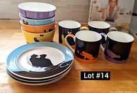 Photo showing the dish set arranged with plates, bowls, and mugs in blue, orange, yellow, and purple colors with cat silhouette designs.