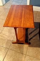 Full view of a rectangular wooden end table with a smooth surface and visible grain, standing on a tiled floor.