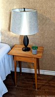 Wooden end table with a lamp and small plant on top, showing the tabletop and four legs.