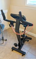 Stationary exercise bike with black frame, display screen, handlebars, and orange resistance bands from an angled top front view.