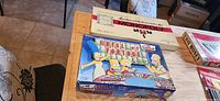 Photo showing Monopoly, Wheel of Fortune Simpsons Edition, and The Game of Easy Money board game boxes arranged on a table.