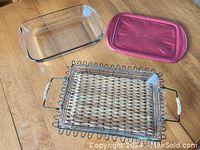 Two large clear glass baking dishes, one smaller glass dish with pink plastic lid, metal carrier rack and utensils on wood surface.