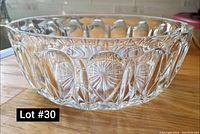 Clear glass or crystal bowl with oval and starburst cut pattern shown from side angle on wooden surface.