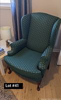Photo of a green wingback chair showing fabric upholstery with circular pattern and wooden Queen Anne-style legs.